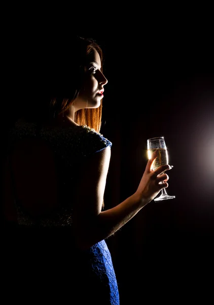 Jovem celebrando mulher em um vestido azul segurando uma taça de champanhe em um fundo escuro. jogo de luz e shedow — Fotografia de Stock