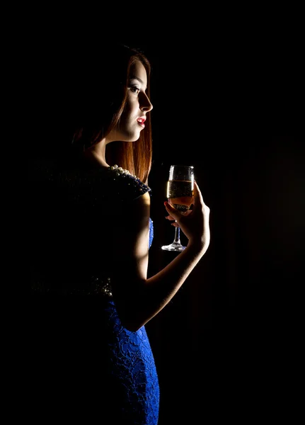 Unga firar kvinnan i en blå klänning som håller ett glas champagne på en mörk bakgrund. spel av ljus och shedow — Stockfoto