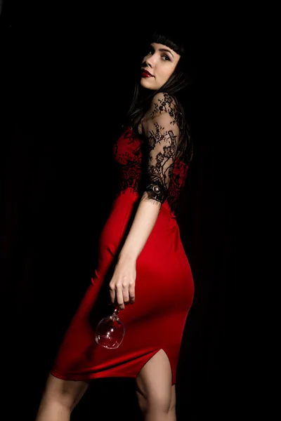 Giovane donna celebrante in abito rosso con un bicchiere che esce dall'oscurità . — Foto Stock