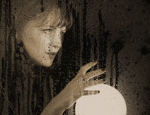 Kadın modeli düzgün portresi, şeffaf cam arkasında poz su damlaları ile kaplı. kadın holding büyük parlayan top — Stok fotoğraf