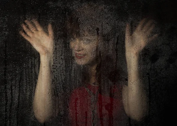 Retrato liso de modelo femenino, posando detrás de vidrio transparente cubierto por gotas de agua. joven mujer sonriente retrato —  Fotos de Stock