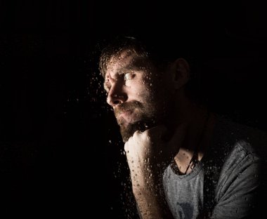 Karanlık ile korkunç sakallı adam portresi sırıtıp, farklı duygular ifade eder. Bir cam, el ve erkek yüz su damlaları