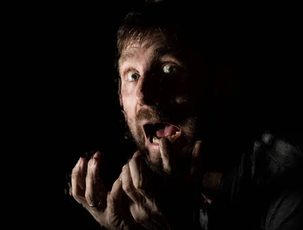 Тёмный портрет страшного бородатого человека с ухмылкой, выражает различные эмоции. Капли воды на стекло, руку и мужское лицо — стоковое фото