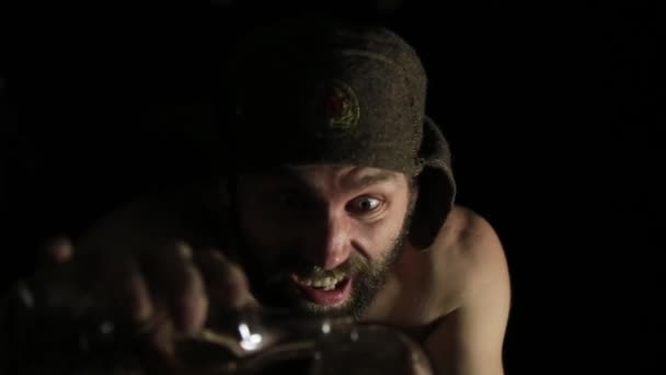 Eng kwaad sinistere bebaarde man met grijns, met een fles van wijnstokken en glas. vreemde Russische man met een naakte torso en een wollen hoed — Stockvideo