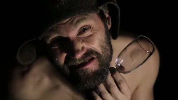 Félelmetes gonosz baljós szakállas férfi önelégült mosoly, szőlő- és üveg tart. furcsa orosz ember meztelen felsőtestét, és egy gyapjú sapka — Stock videók