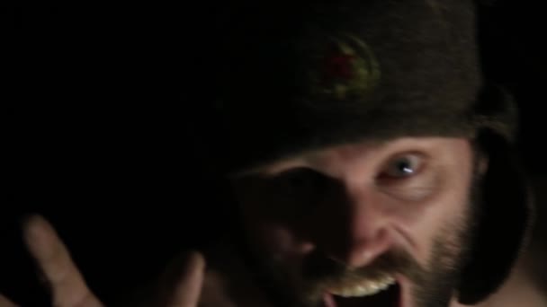 Eng kwaad sinistere bebaarde man met grijns, springt abrupt uit de duisternis. vreemde Russische man met een naakte torso en een wollen hoed — Stockvideo