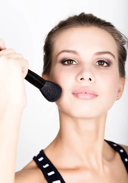 Close-up Female model applying makeup on her face. Beautiful young woman applying foundation on her face with a make up brush. — Stock Photo, Image