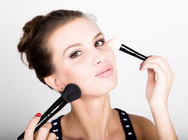 Yakın çekim kadın modeli yüzünde makyaj uygulamak. Yüzünü bir makyaj fırça ile vakıf uygulayarak güzel genç kadın.