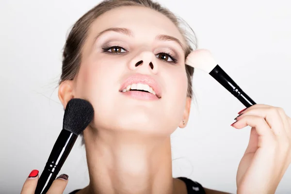 Close-up Female model applying makeup on her face. Beautiful young woman applying foundation on her face with a make up brush. — Stock Photo, Image