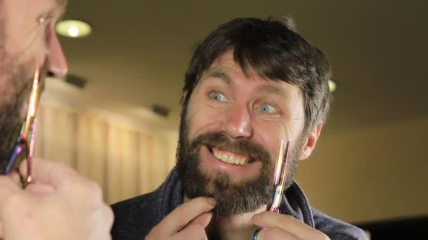 Close-up Young Handsome man trimming beard with scissors. Young man in beauty saloon working on his beard and styling with comb and scissors. — Stock Video