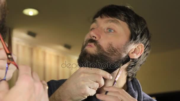 Gros plan Jeune homme beau taille barbe avec des ciseaux. Jeune homme dans le salon de beauté travaillant sur sa barbe et son style avec peigne et ciseaux . — Video
