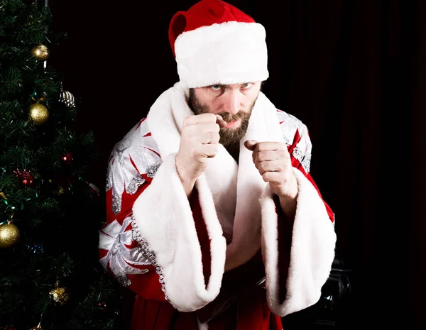 Bad brutal Santa Claus clenched his fists, ready to fight on the background of Christmas tree — Stock Photo, Image