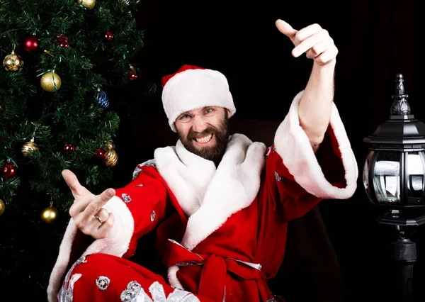 クリスマス ツリーの背景に悪い残忍なサンタ クロース笑顔と示す中指サインします。 — ストック写真