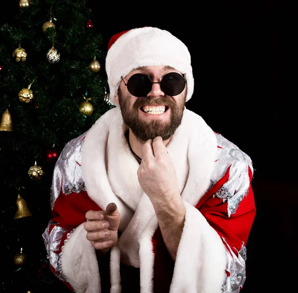 Cattivo rastoman Babbo Natale tenendo la borsa con regali e graffiando la barba sullo sfondo dell'albero di Natale — Foto Stock