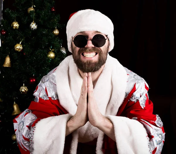 Cattivo rastoman Babbo Natale sorride e rendendo le mani segno namaste sullo sfondo dell'albero di Natale — Foto Stock