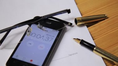 Bir smartphone cep telefonu ile saat ve kronometre yakından görünümü. bir adam bir kronometre başlatır. gözlük ve dolma kalem iş belgeler üzerinde yalan