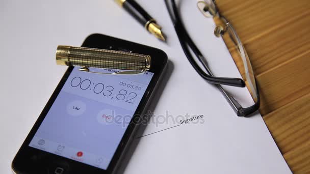 View of close up clock and stopwatch on a smartphone. man starts a stopwatch. glasses and fountain pen lie on the business documents — Stock Video