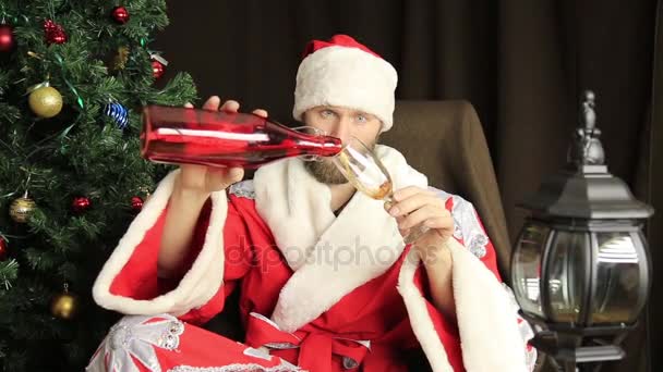 Mal brutal Santa Claus beber vino y dice felicitaciones en las vacaciones, en el fondo del árbol de Navidad — Vídeo de stock