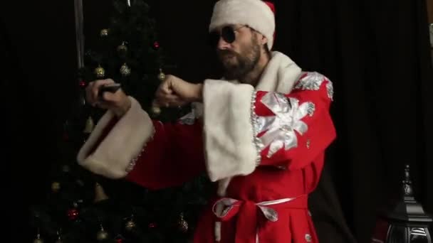 Mal brutal Santa Claus sonriente y divertido baile, en el fondo del árbol de Navidad — Vídeos de Stock