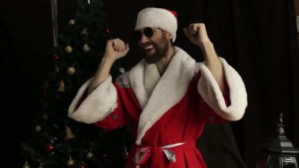 Slechte brute Kerstman glimlachend en grappig dansen, op de achtergrond van de kerstboom — Stockvideo