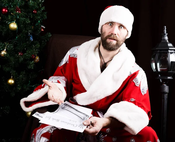 悪い残忍なサンタ クロースが運んでクリスマス ツリーの背景に、願いの手紙を読み取ります — ストック写真