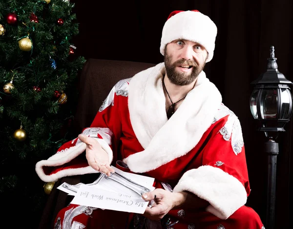 Cattivo brutale Babbo Natale legge malcontento lettera con i desideri, sullo sfondo dell'albero di Natale — Foto Stock