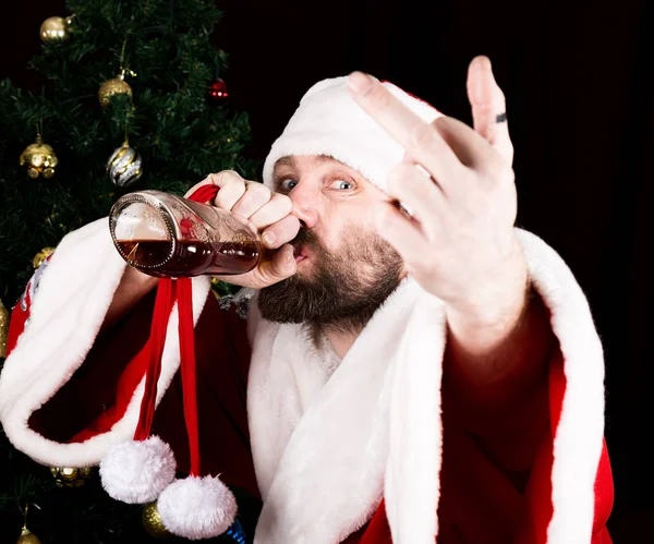 Rău brutal Moș Crăciun zâmbind răutăcios, bând coniac dintr-o sticlă și braț întins, pe fundalul pomului de Crăciun — Fotografie, imagine de stoc