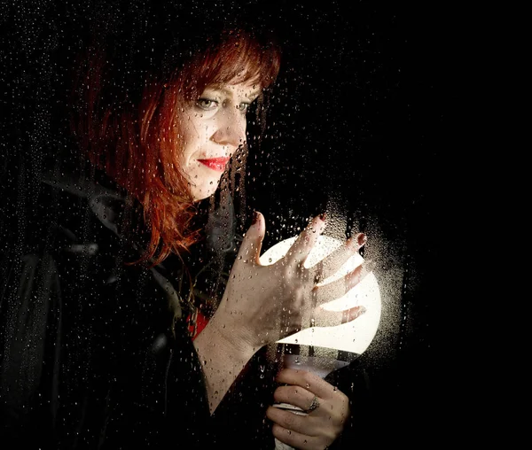 Portrait de modèle féminin, posé derrière un verre transparent recouvert de gouttes d'eau. femme tenant une grosse boule lumineuse — Photo