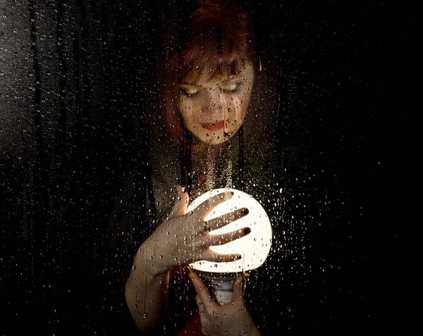 Retrato de modelo femenino, posando detrás de vidrio transparente cubierto por gotas de agua. mujer sosteniendo gran bola brillante — Foto de Stock