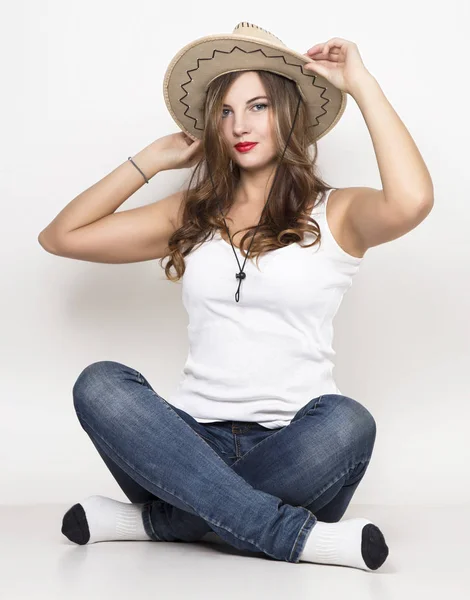 Hermosa chica rizada en jeans, camiseta blanca y sombrero de vaquero . — Foto de Stock