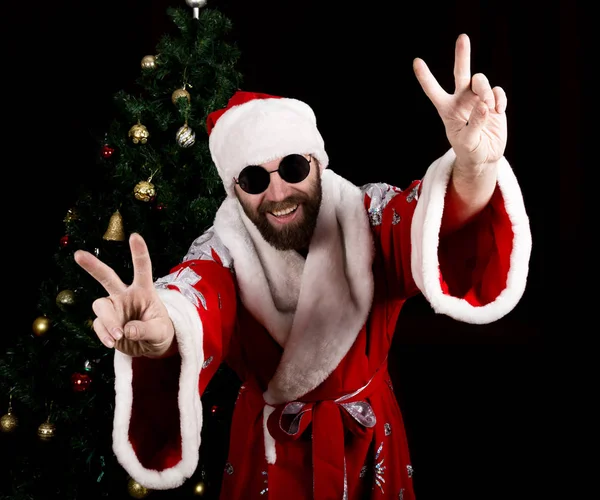 Bad brutal Santa Claus smiles and showing finger sign on the background of Christmas tree — Stock Photo, Image