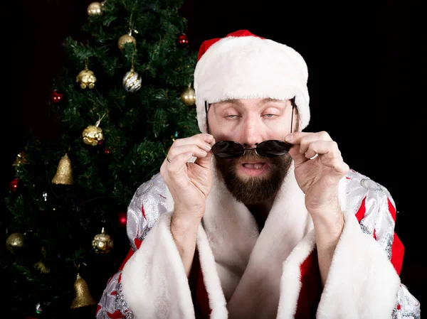 悪い rastoman サンタ クロースは、クリスマス ツリーの背景に、微笑みと丸いメガネを保持します。異なる funy 感情 — ストック写真