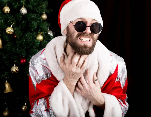 Rossz rastoman Mikulás ajándékokat szütyőt és vakarja a szakállát, a háttérben a karácsonyfa — Stock Fotó