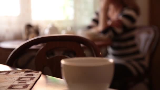 Młoda kobieta, siedząc w kawiarni, picie herbaty lub kawy i uśmiechając się — Wideo stockowe
