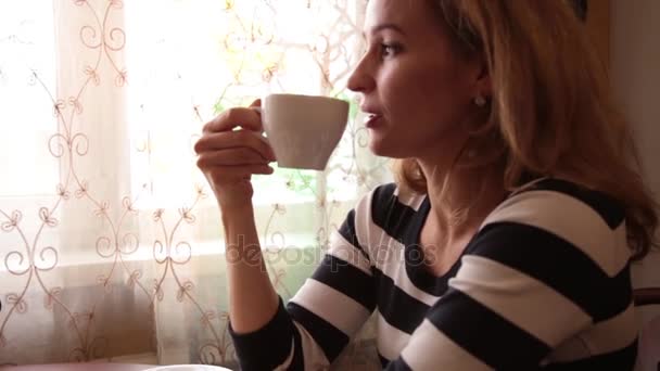 Pretty young woman sitting at cafe drinking tea or coffe and smiling — Stock Video