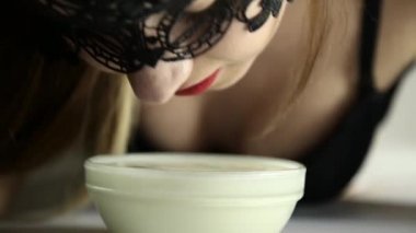 Close-Up bir kedi gibi süt içme dantel maskeli genç seksi bir kadın. gülümseyen kız lepleme yoğurt cam kase