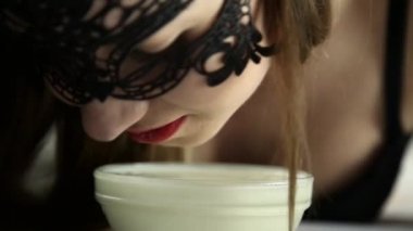 Close-Up bir kedi gibi süt içme dantel maskeli genç seksi bir kadın. gülümseyen kız lepleme yoğurt cam kase