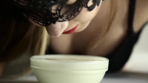 Primo piano di una giovane donna sexy con una maschera di pizzo che beve latte come un gatto. sorridente ragazza lappatura yogurt da ciotole di vetro — Video Stock