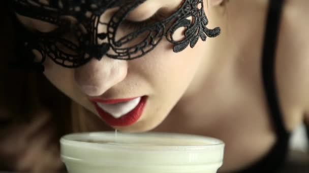 Close-up van een jonge sexy vrouw in een masker van de kant consumptiemelk als een kat. lachende meisje kabbelende yoghurt uit glazen kommen — Stockvideo