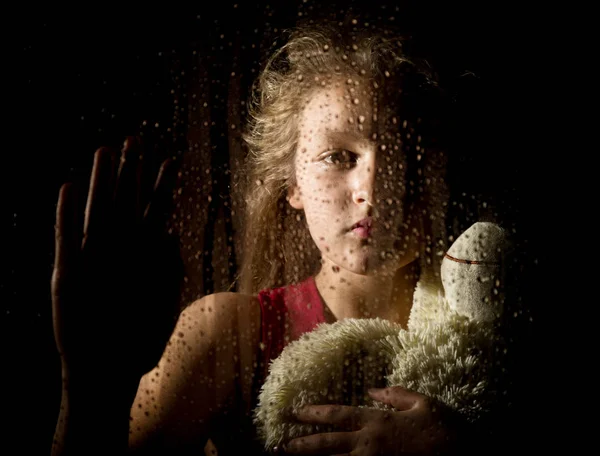 Μοναχικό νεαρό θλιβερή κορίτσι πίσω από το παράθυρο με σταγόνες, κρατώντας αρκουδάκι και κλαίει — Φωτογραφία Αρχείου