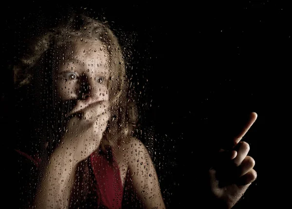Μοναχική κοπέλα θλιβερό πίσω από το παράθυρο με σταγόνες. φοβισμένη νεαρή γυναίκα δείχνει κάτι — Φωτογραφία Αρχείου