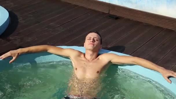 Красивый мужчина расслабляется в джакузи рядом с бассейном — стоковое видео