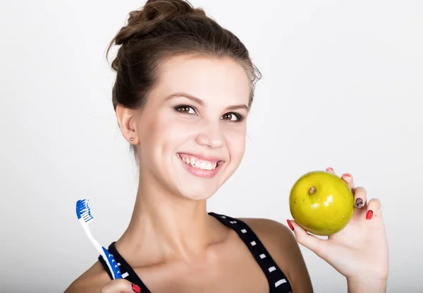 Retrato de una mujer joven sosteniendo una manzana y un cepillo de dientes, concepto de salud dental — Foto de Stock