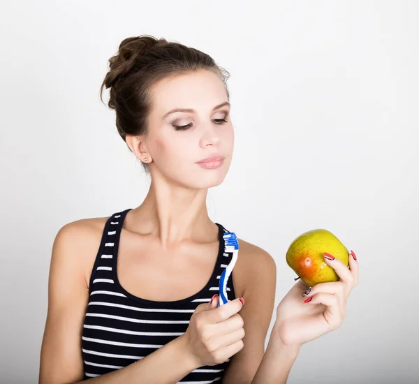 Retrato de una mujer joven sosteniendo una manzana y un cepillo de dientes, concepto de salud dental — Foto de Stock