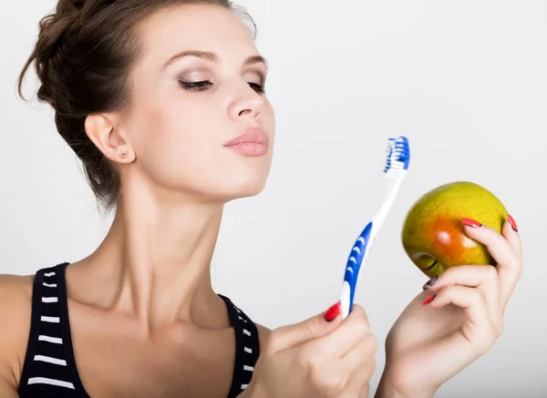 Retrato de una mujer joven sosteniendo una manzana y un cepillo de dientes, concepto de salud dental — Foto de Stock