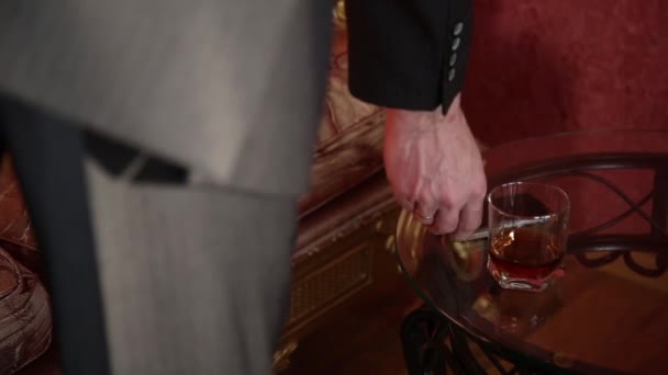 Hombre de negocios beber brandy y pone el vaso en la mesa de café — Vídeos de Stock