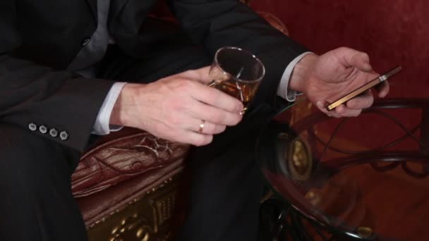 Hombre de negocios bebiendo brandy, pone el vaso en la mesa de café e irritablemente llama por teléfono — Vídeo de stock