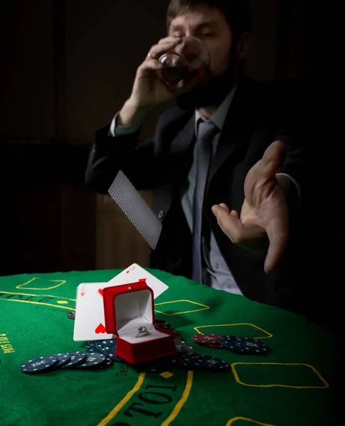 Vício em jogo. homem em um terno de negócios bebendo conhaque e joga cartas com combinação perdedora. fichas de casino, anel precioso na mesa de poker verde — Fotografia de Stock