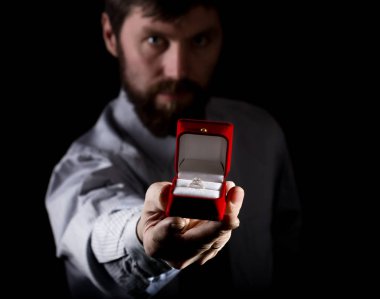 bearded man in business suit gives a ring in the red box and expresses different emotions on dark background clipart