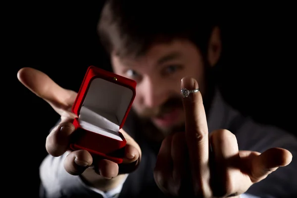 Uomo barbuto in abito da lavoro dà un anello nella scatola rossa e mostrando dito medio su sfondo scuro — Foto Stock